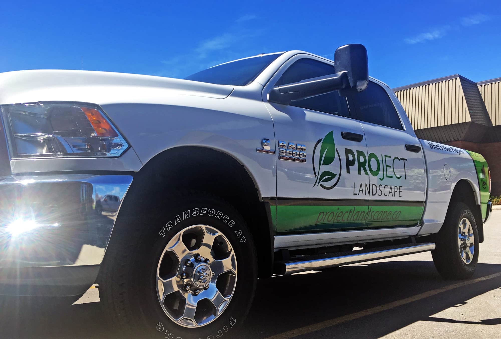 A partial vinyl vehicle wrap, company logo decals, and phone number decals on a company work Dodge pickup truck.