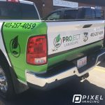 A partial vinyl vehicle wrap, company logo decals, and phone number decals on a company work Dodge pickup truck.