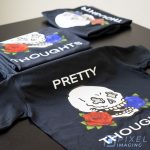 Several custom-printed heat-press vinyl T-shirts featuring a skull with blue and red roses bearing the text "pretty thoughts."
