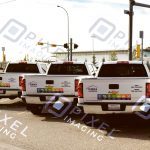 Custom-printed company logo decals and phone number vinyl lettering on company pickup truck fleet.